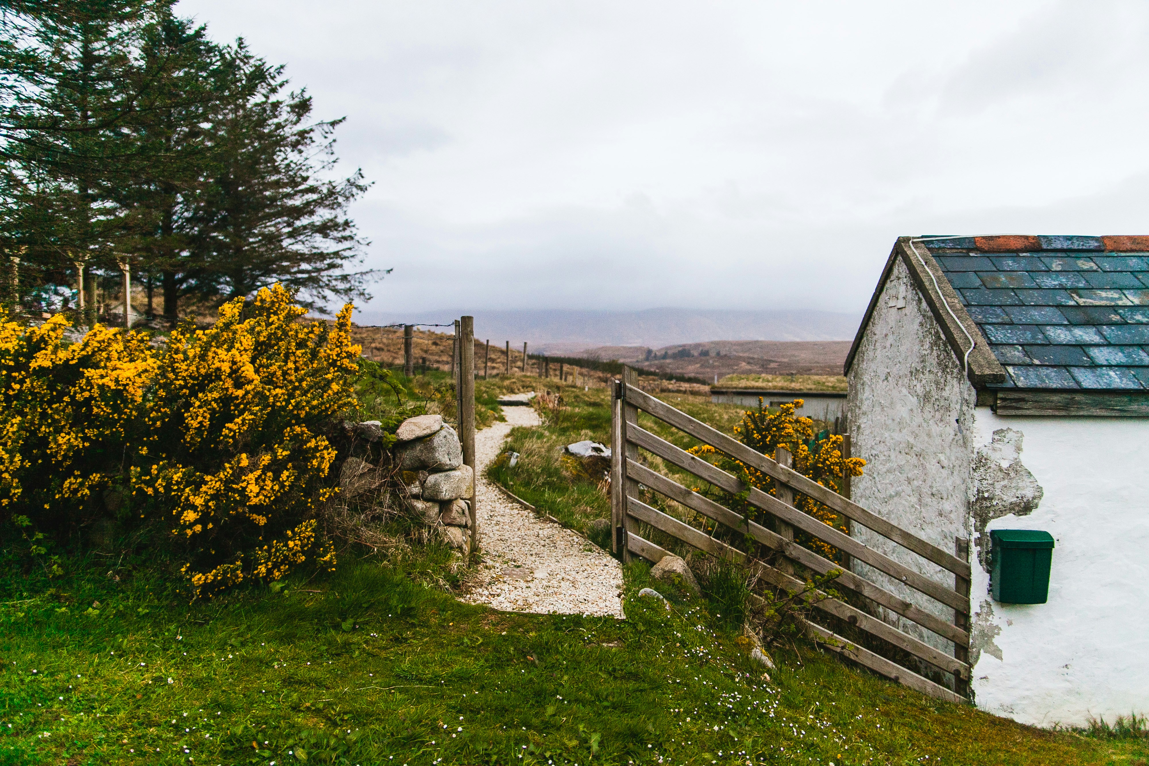 A landscape of the English countryside showing some flowers, a gated entry, and a small stone house. 